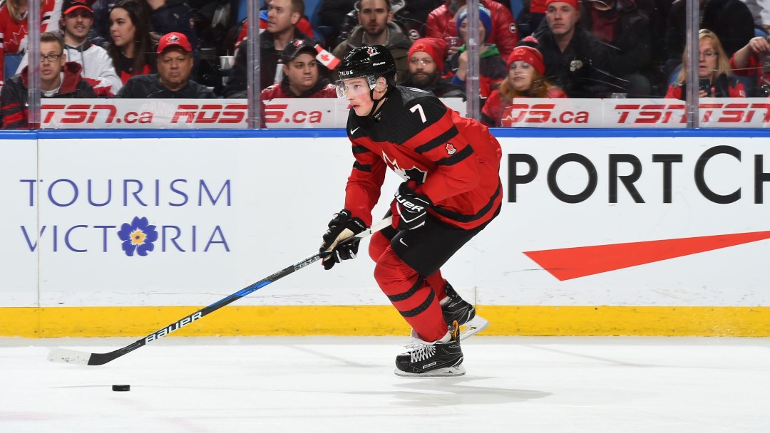 Cale Makar skates with the puck by his stick, wearing a red jersey