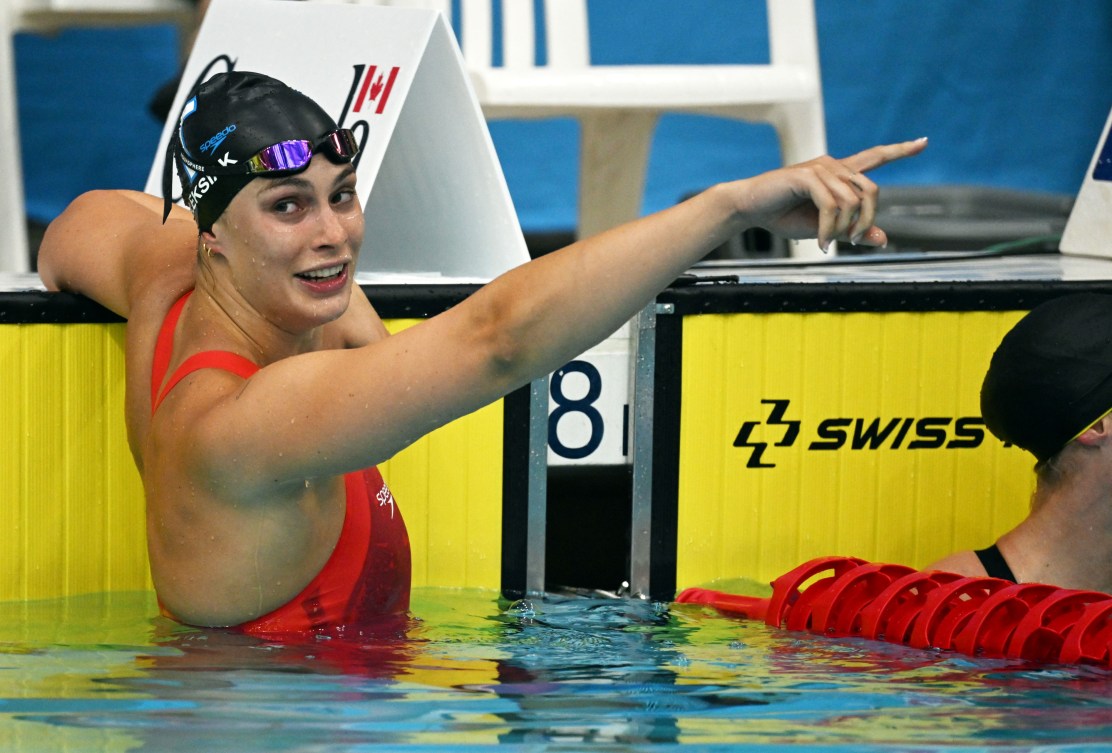 Penny Oleksiak points to something as she hangs off the pool wall 