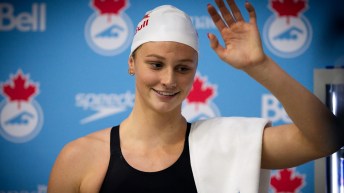 Summer McIntosh waves while standing in front of a blue banner