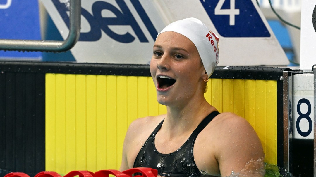 Summer McIntosh wearing a white cap and black suit smiles at the end of the pool