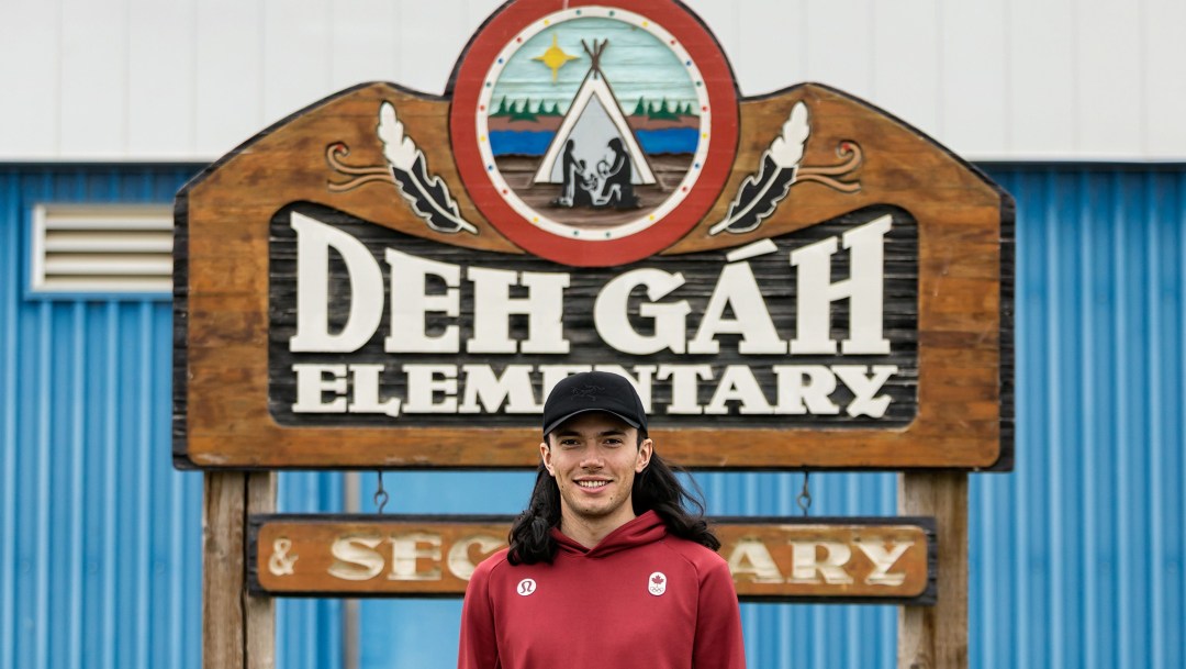 Liam Gill stands in front of a sign for Deh Gah Elementary and Secondary School