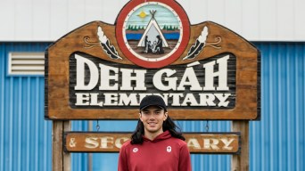 Liam Gill stands in front of a sign for Deh Gah Elementary and Secondary School