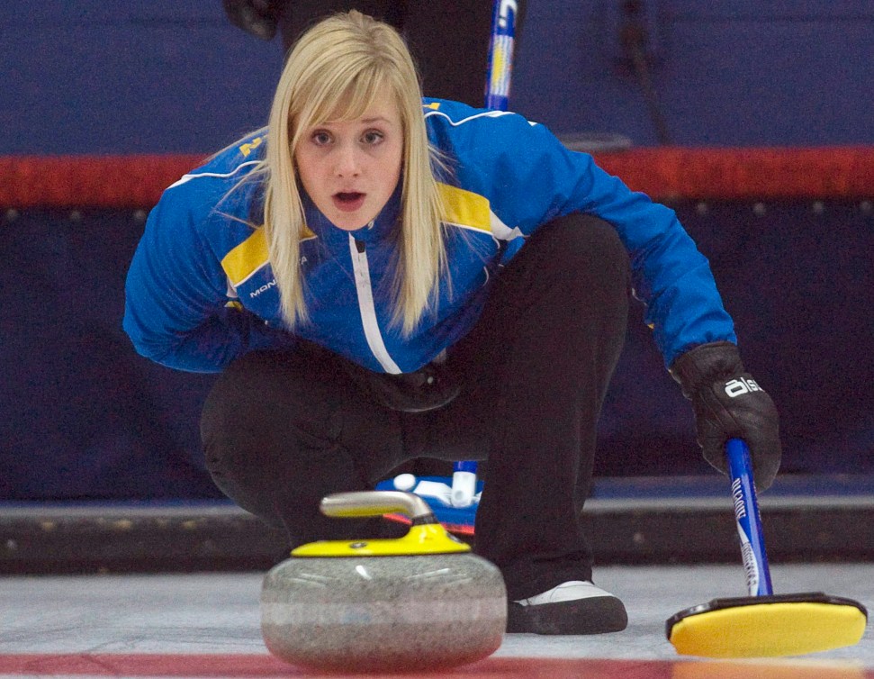 Jocelyn Peterman in a blue jacket squats behind a yellow curling stone