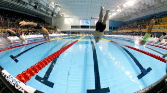 Fish eye lens view of swimmers diving into pool from start blocks