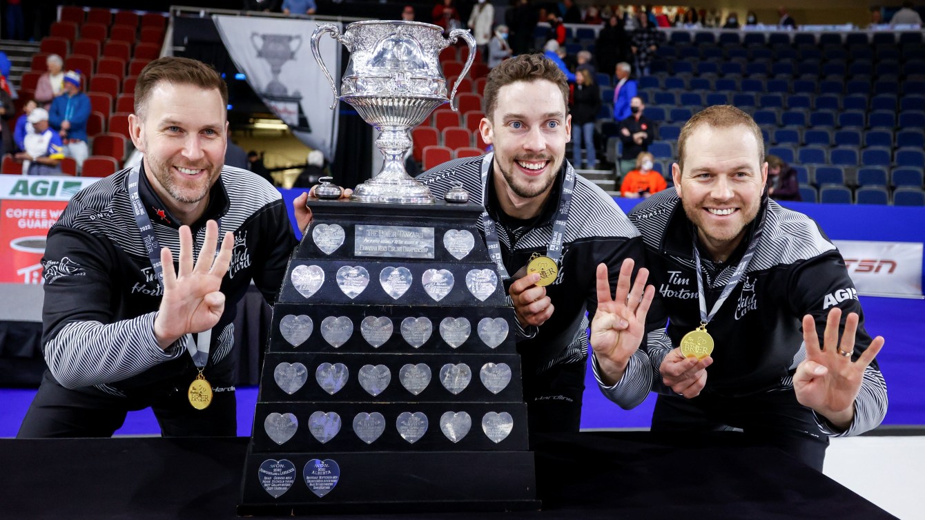 Three curlers dressed in black pose behind a trophy showing four fingers each