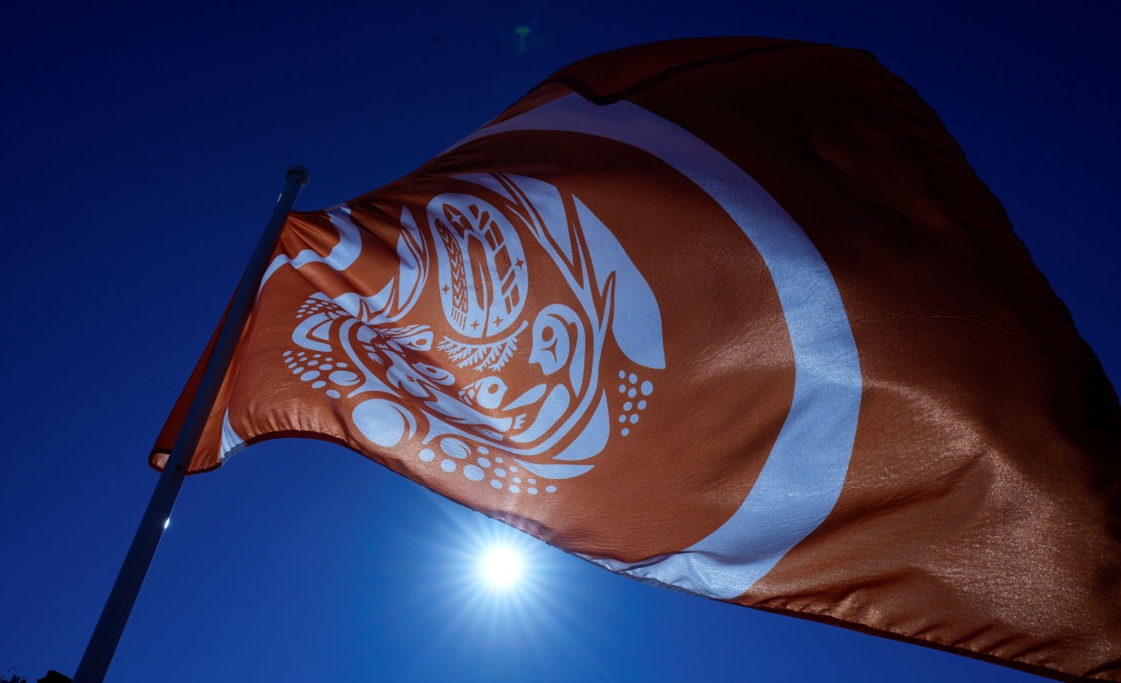 Orange flag with white Indigenous design flies against a blue sky 