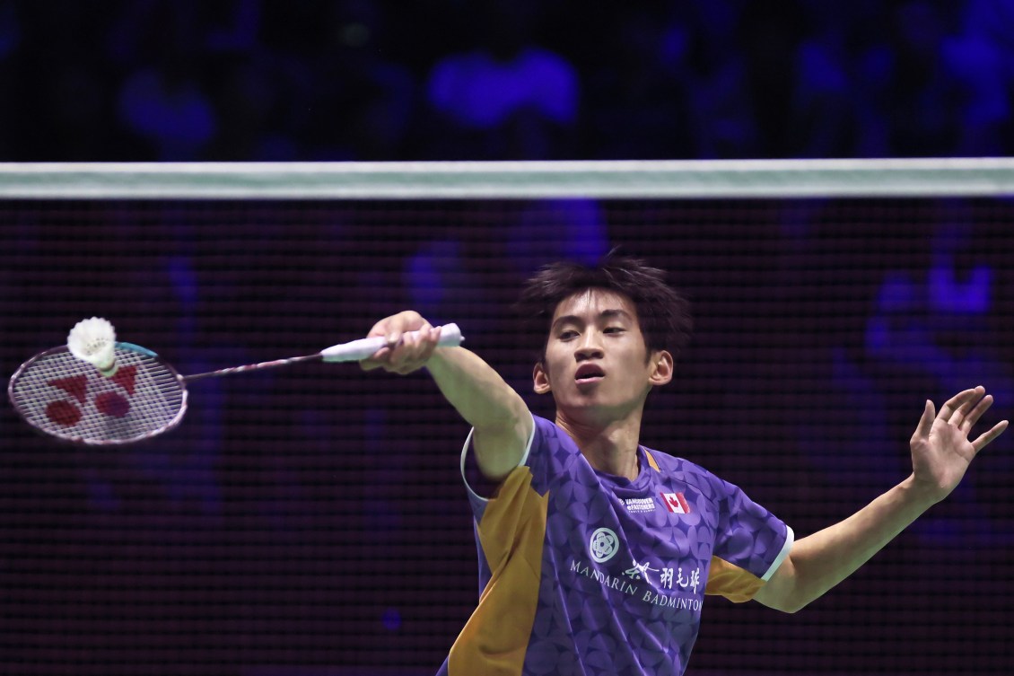 Victor Lai in a purple shirt hits a forehand in badminton