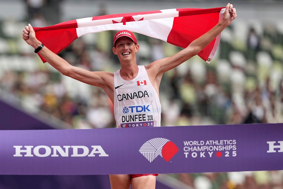 Evan Dunfee holds the Canadian flag above his head as he walks into the purple banner marking the finish line