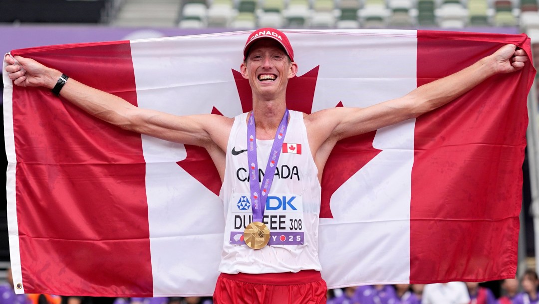 Evan Dunfee holds the Canadian flag behind him while wearing a gold medal over his white singlet