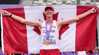 Evan Dunfee holds the Canadian flag behind him while wearing a gold medal over his white singlet