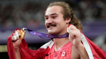 Ethan Katzberg holds his gold medal with a Canadian flag draped over his shoulders