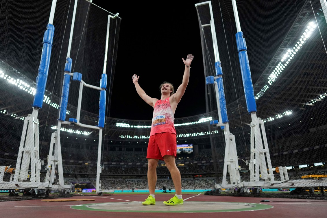 Ethan Katzberg raises his arms in celebration standing inside the hammer throw cage