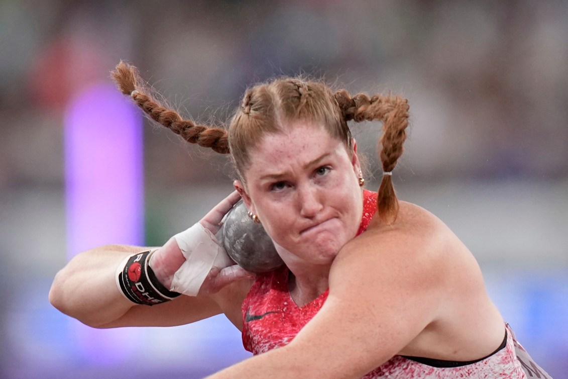 Sarah Mitton with her red hair in two braids prepares to throw the shot put with it nestled in her neck