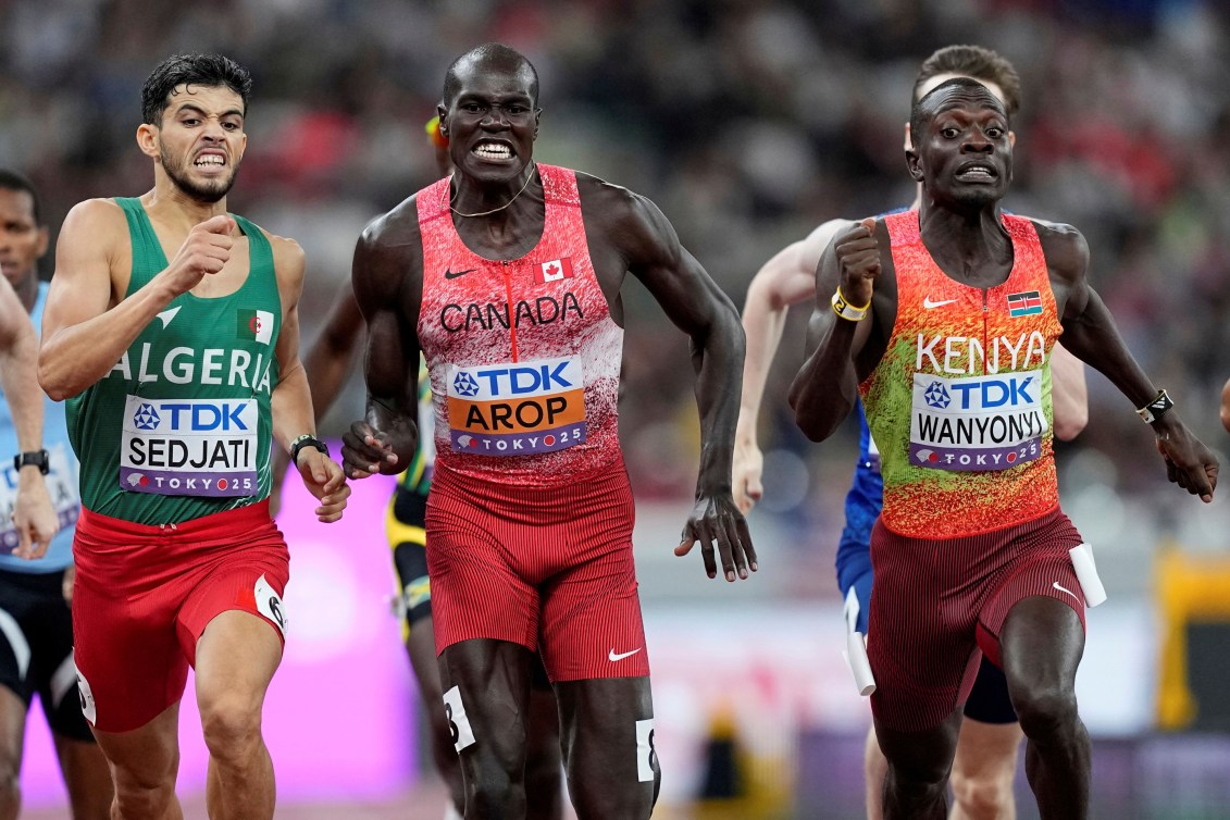 Three men run with anguished faces toward the camera and the finish line