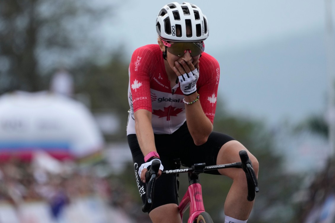 Wearing a red and white road cycling suit, Magdeleine Vallieres puts her hand over her mouth in surprise and shock 