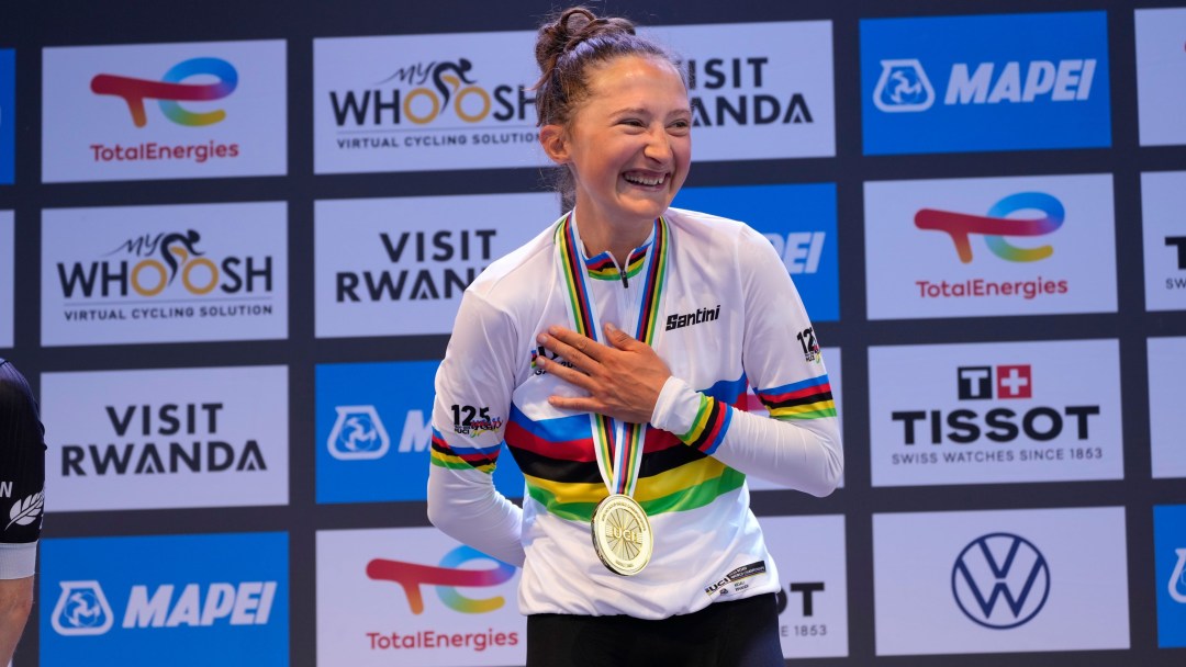 Magdeleine Vallieres wears the rainbow jersey and gold medal on the medal, laughing as she holds her hand over her heart