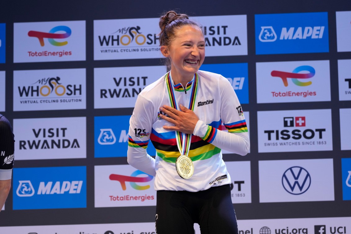 Magdeleine Vallieres wears the rainbow jersey and gold medal on the medal, laughing as she holds her hand over her heart