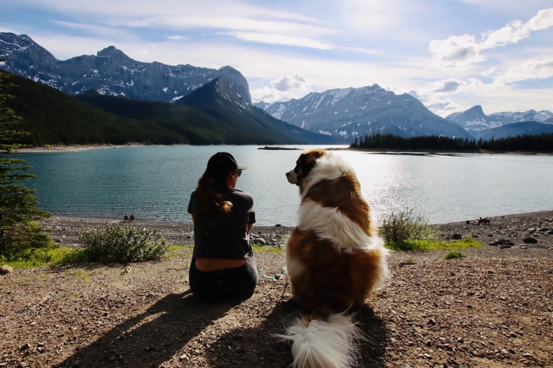 Ivanie Blondin sits beside her dog looking out over a lake and mountains