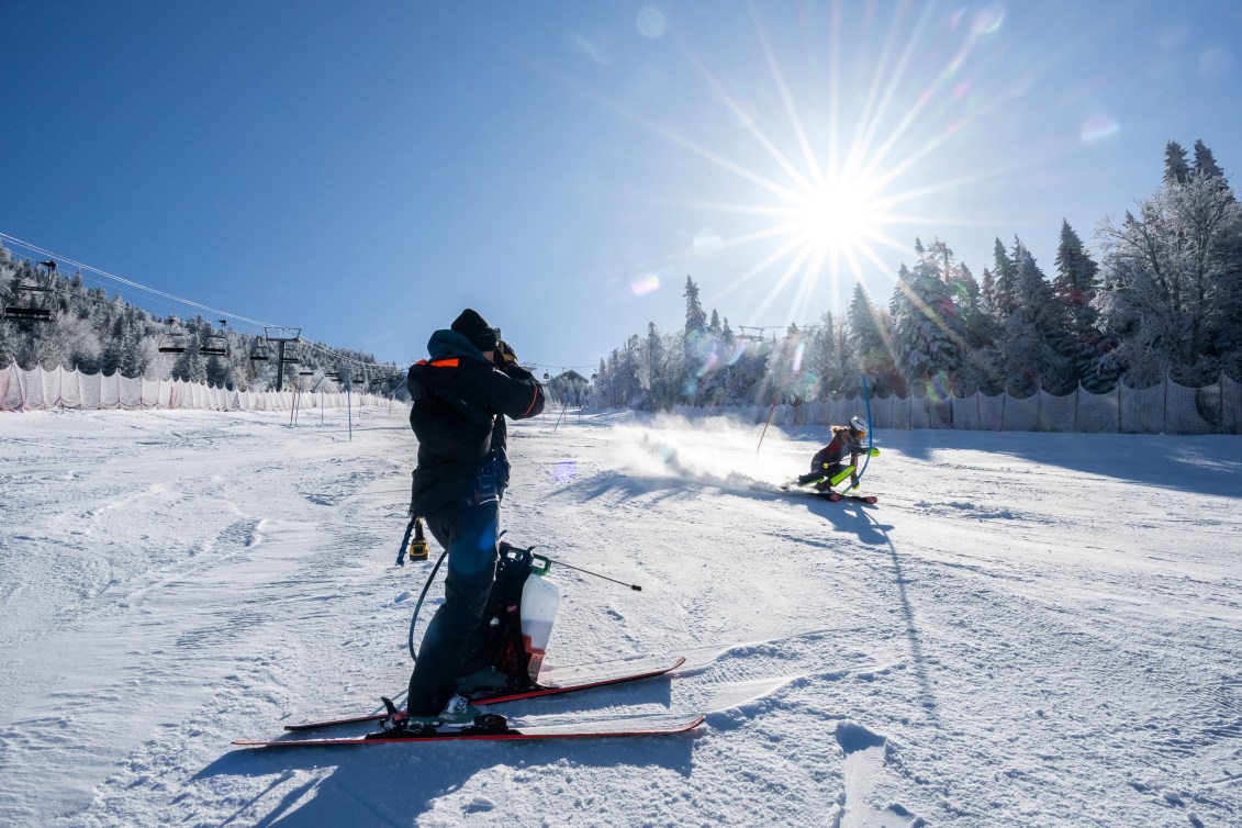 A coach watches while her skier goes down the slope