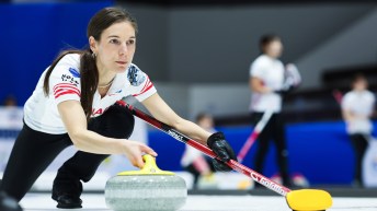 Rachelle Brown in white shirt and black pants slides to throw a curling stone