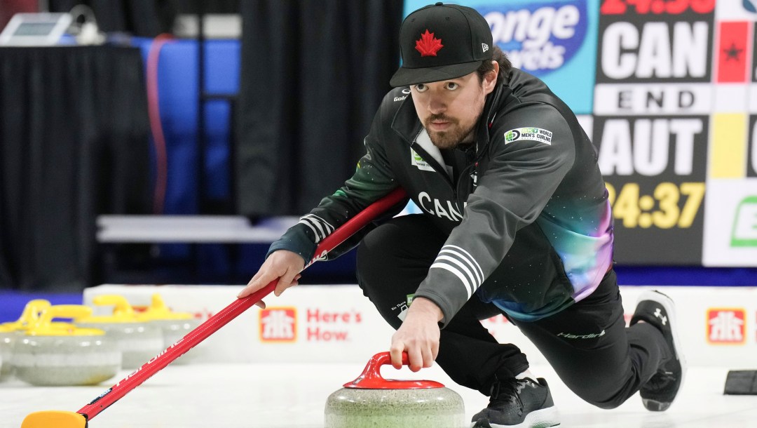 Tyler Tardi dressed in black jacket and pants slides to throw a curling stone
