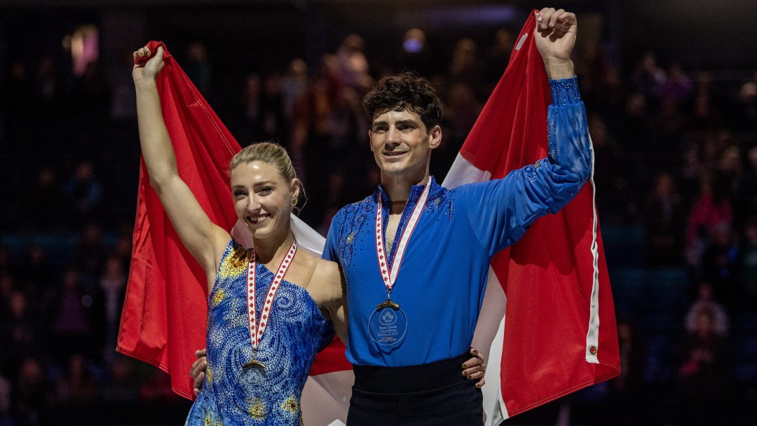 Dressed in blue outfits, Piper Gilles and Paul Poirier hold a Canadian flag behind them