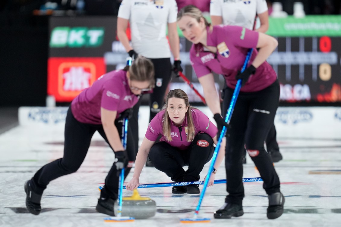 Curler in magenta shirt has just thrown a stone which is being swept by her teammates