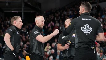 Four male curlers dressed in black fist pump each other