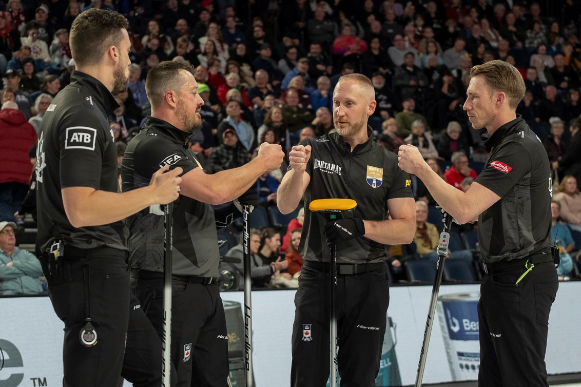Four male curlers dressed in black pump each other's fists