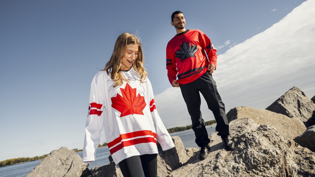 A woman wearing a red and white Team Canada hockey jersey and a man wearing a red and black Team Canada hockey jersey stand on rocks