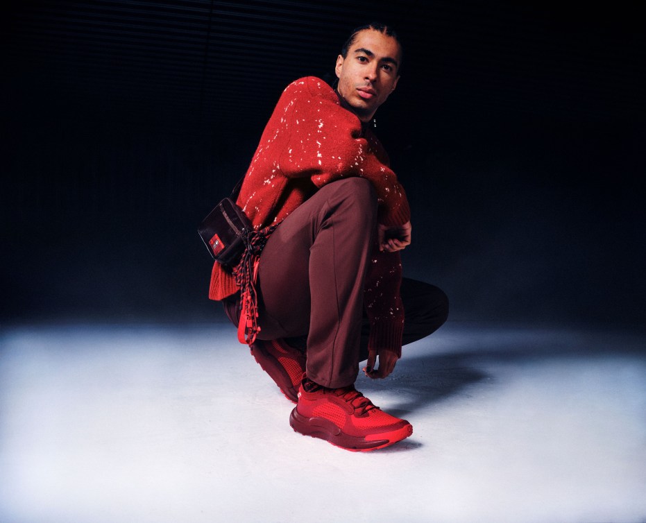 William Dandjinou crouches in a red sweater and burgundy pants