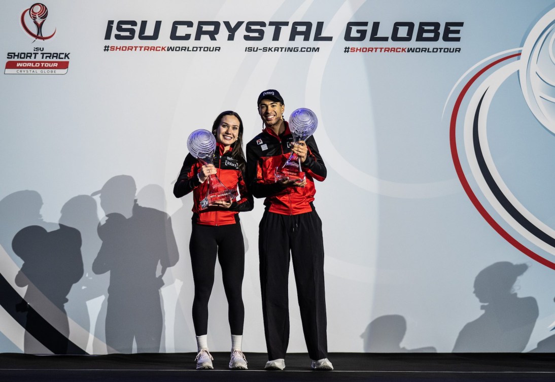 Courtney Sarault and William Dandjinou dressed in red and black jackets hold crystal globe trophies