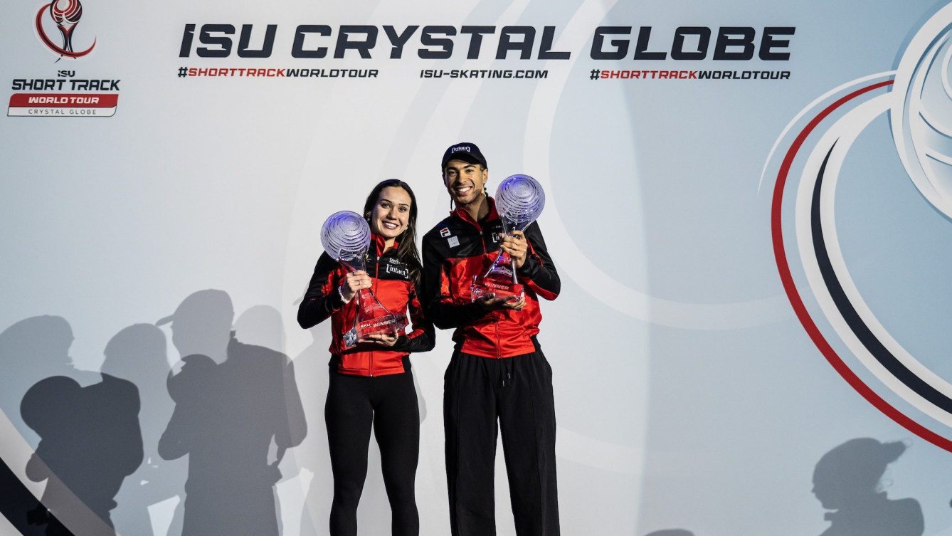 Courtney Sarault and William Dandjinou dressed in red and black jackets hold crystal globe trophies