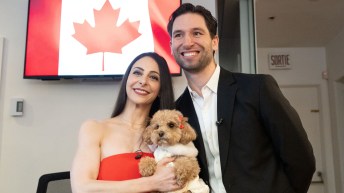 Deanna Stellato-Dudek in a red strapless dress holds her small dog in her arms with partner Maxime Deschamps just behind her