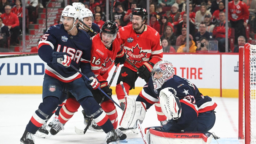 Two Canadian players in red uniforms battle American players in navy blue