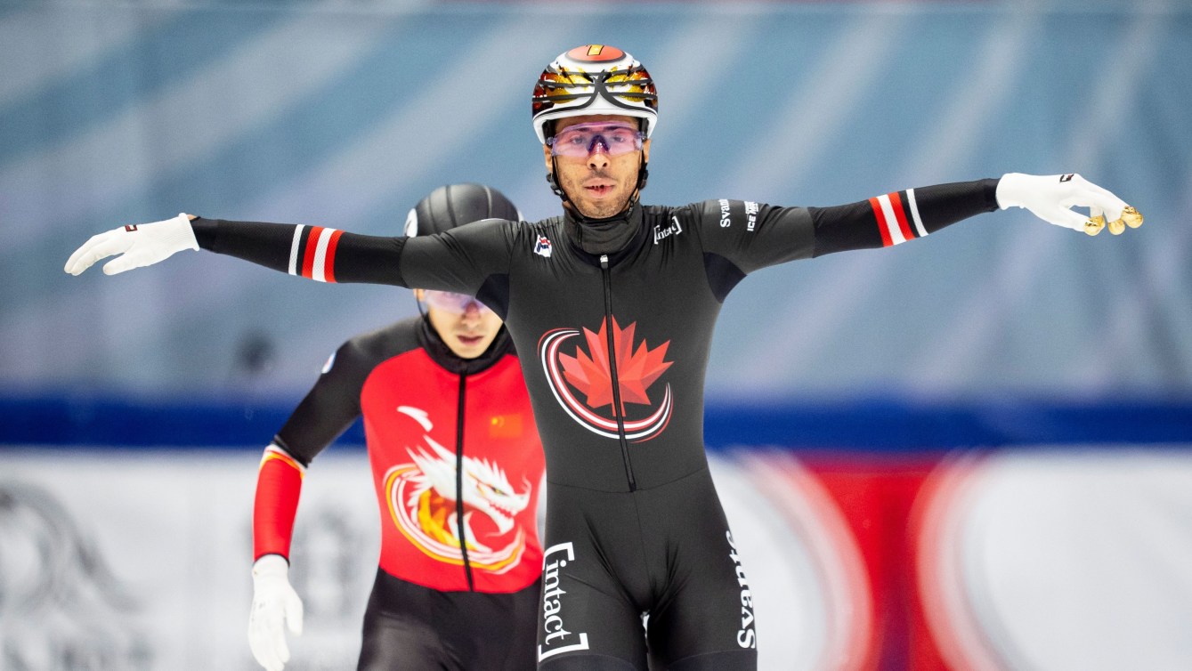 William Dandjinou in black skin suit with maple leaf on chest flaps his arms out wide