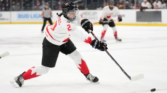 Female hockey player in white jersey and black shorts hits a slapshot on a puck