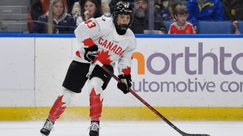 Female hockey player in white jersey with red maple leaf prepares to shoot a puck