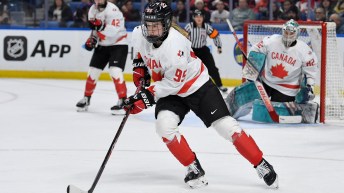 Female hockey player in white jersey with red maple leaf skates with puck on stick blade