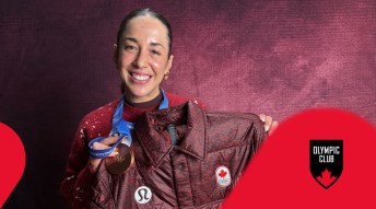 Valerie Maltais holding a burgundy signed jacket wearing bronze medal.