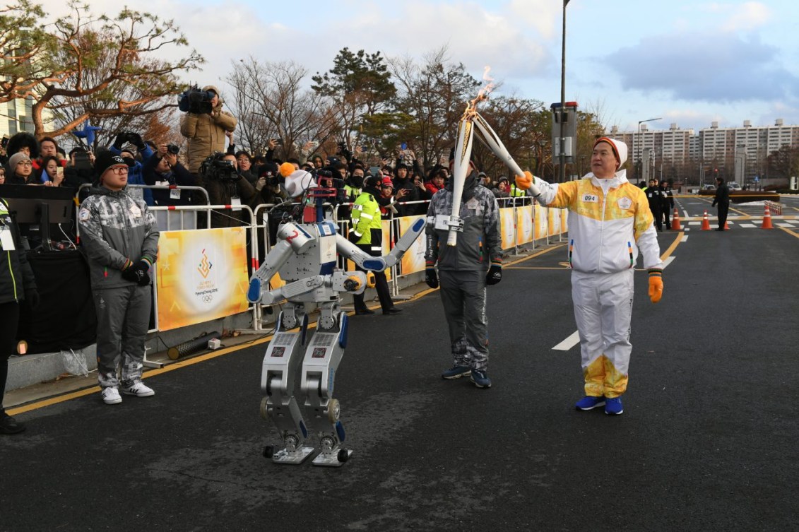 Un relayeur passe la flamme olympique à un robot