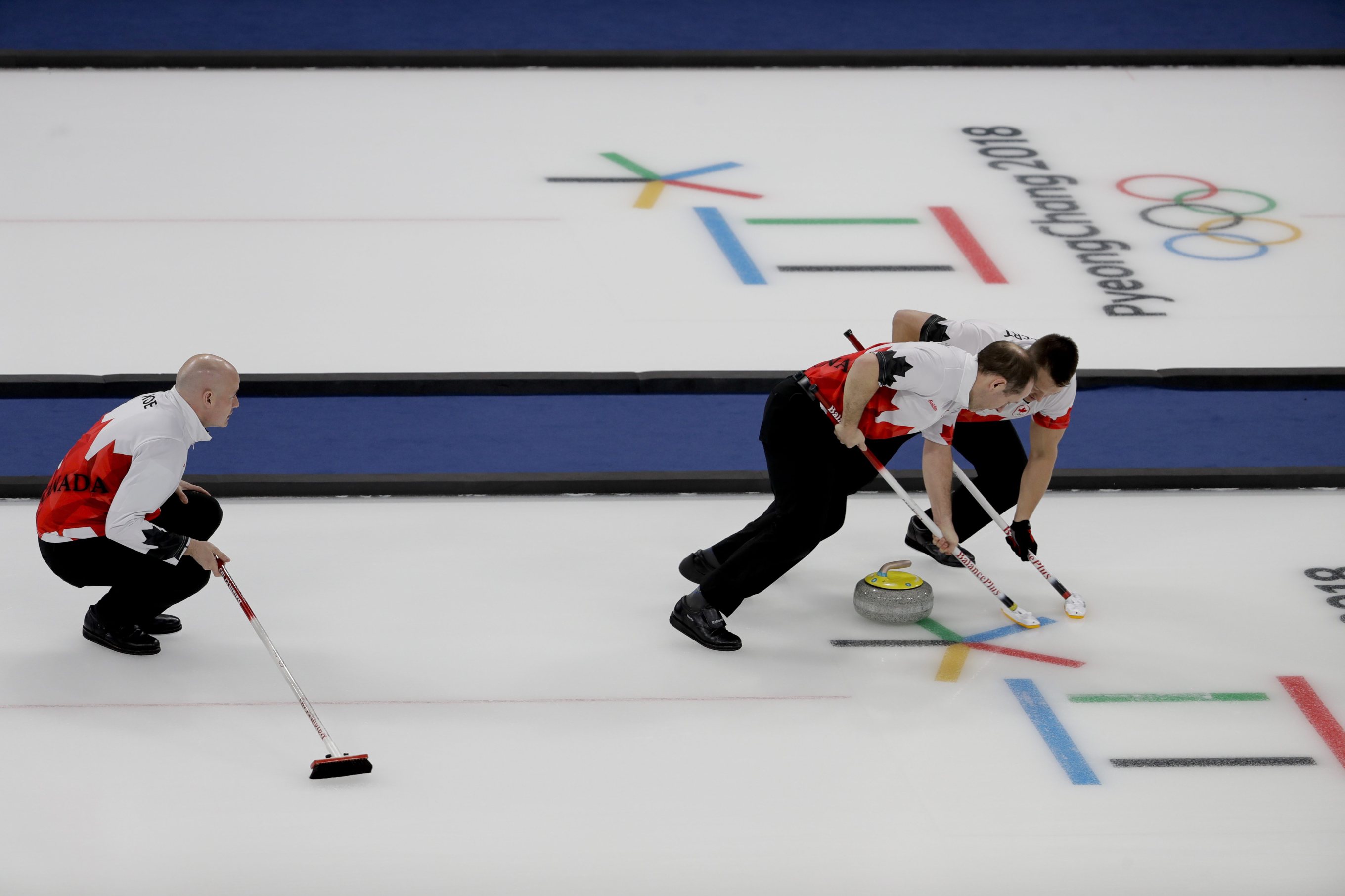 Le capitaine du Canada, Kevin Koe, observe ses coéquipiers Ben Hebert, à droite, et Brent Laing balayant pendant un match de curling contre le Japon lors des Jeux olympiques d'hiver de PyeongChang à Gangneung en Corée du Sud, le mardi 20 février 2018. (Photo : AP/Natacha Pisarenko)