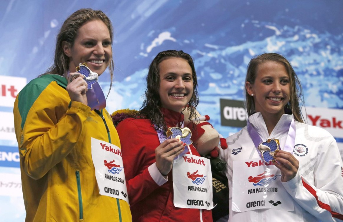 Kylie Masse, au centre, célèbre sur le podium après avoir gagné au 100 m dos en compagnie de Emily Seebohn, à gauche, et de Kathleen Baker, à droite, aux Championnats pan-pacifiques à Tokyo. Vendredi 20 août 2018. (AP Photo/Koji Sasahara)